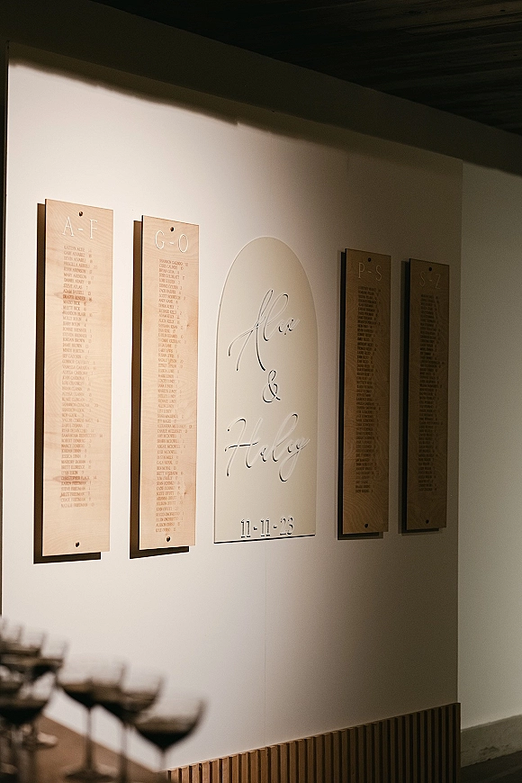 Seating chart display with vertical wood boards and an arched acrylic name sign, wall-mounted on a clean white wall for a modern look