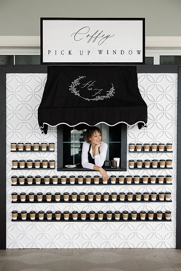 Wedding coffee bar with coffee cups and custom sleeves at a coffee pickup window, featuring a monogrammed black awning and service shelves