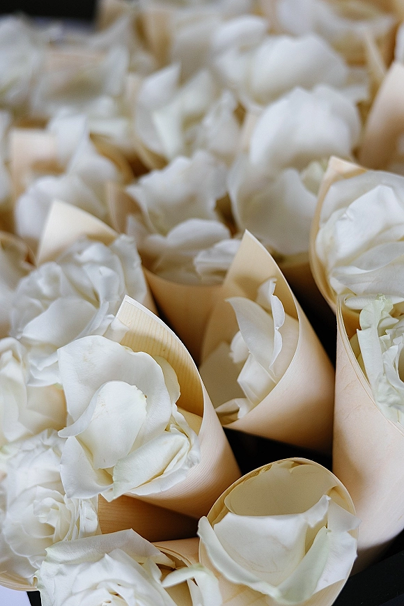 Rose petal confetti with white rose petals filled in paper petal toss cones arranged neatly on a dark surface for a ceremony send-off