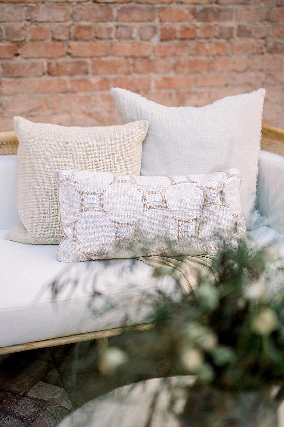 Lounge seating decor with an outdoor sofa and throw pillows arranged on a patio, set against a brick wall with greenery