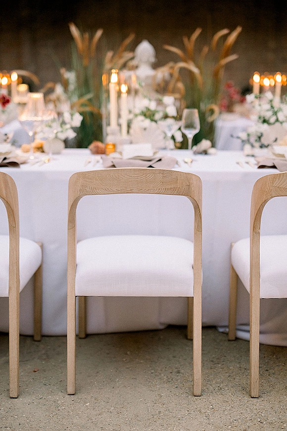 Reception tablescape with white linen reception table, taper candle centerpiece, pampas grass and greenery, glowing against a dark wall backdrop