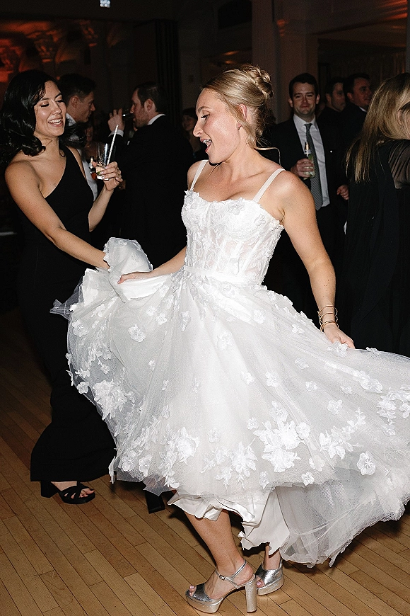 Bride dancing on the wedding reception dance floor, twirling her tulle skirt in low light while guests watch, cocktail glass in hand.