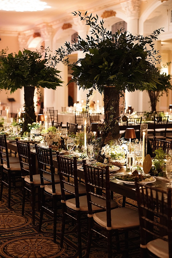 Reception tablescape with greenery wedding tablescape centerpieces, taper candles, mini lamps and formal place settings in a warm-lit ballroom
