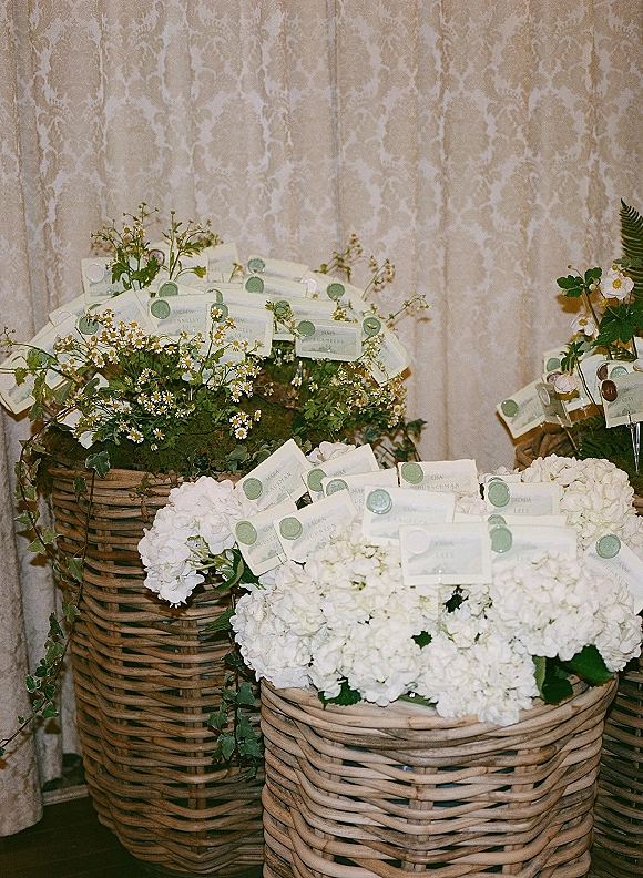 Escort card display with wedding escort cards sealed in green wax, nestled among hydrangeas, daisies, ivy, and wicker baskets
