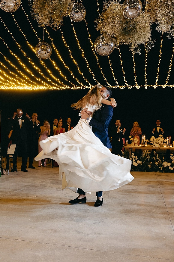 First dance wedding first dance moment as groom spins bride in a twirling gown under string lights and disco balls on an outdoor dance floor at night