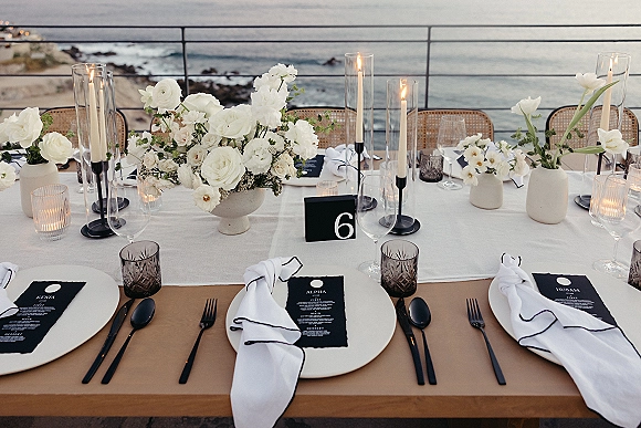 Reception tablescape with coastal wedding tablescape styling, white floral centerpieces and taper candles in hurricanes on an ocean-view terrace