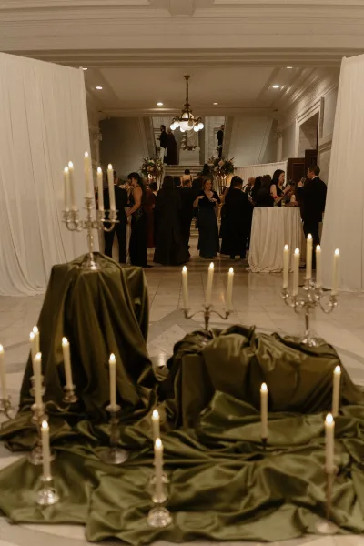 Wedding cocktail hour with candlelit cocktail hour decor, tall tables and floral candelabras beneath a chandelier by a grand staircase foyer