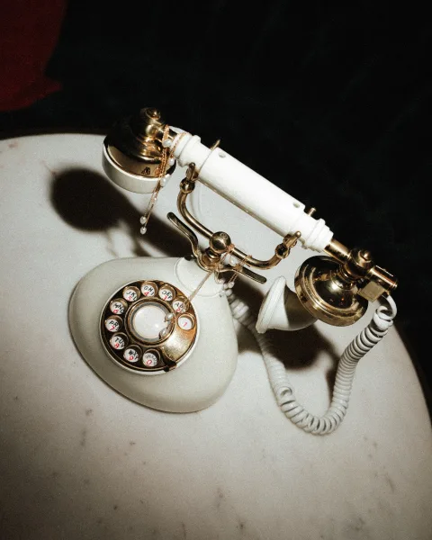 Wedding detail photo of a vintage phone wedding decor flat lay with pearl necklace draped over a white rotary telephone on marble tabletop