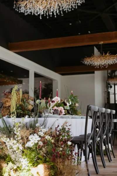 Reception tablescape with wedding head table decor featuring a floral centerpiece and red taper candles beneath a crystal chandelier in an indoor venue