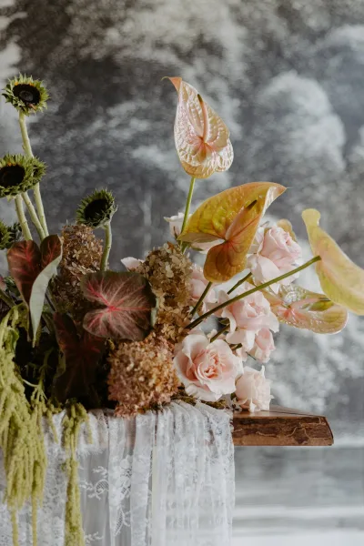Wedding floral arrangement with anthurium, blush roses, sunflowers, and hanging amaranthus on a wooden pedestal against a gray marbled backdrop
