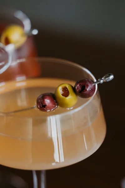 Wedding cocktails with a signature wedding cocktail martini, olive garnish on a cocktail pick in a glass against a dark, moody background
