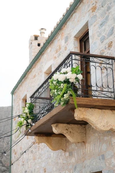 Balcony floral decor featuring white balcony flowers cascading over a wrought iron railing, set against a rustic stone wall and rocky hillside.