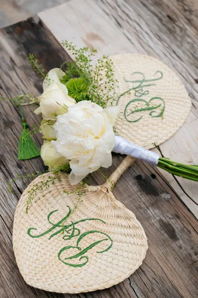 Bridal bouquet, a white peony bouquet accented by woven fans on a weathered wood table of wooden planks.
