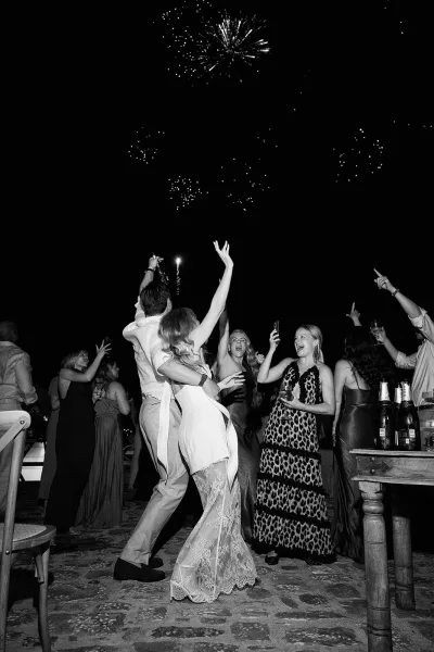 Wedding fireworks moment during a reception dance moment under a night sky, with champagne glasses catching the light on a stone patio.