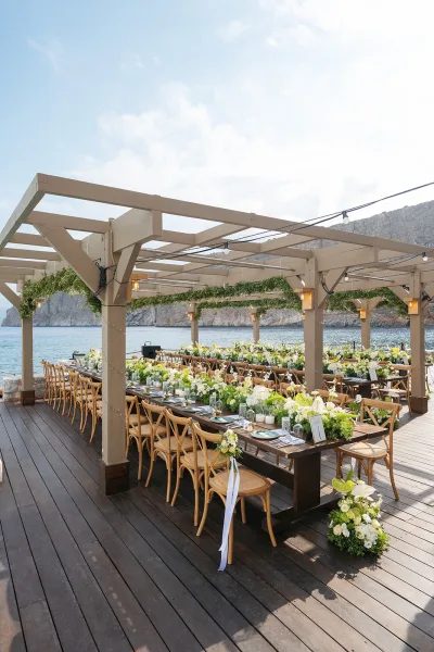 Reception tablescape featuring outdoor reception decor with greenery garlands, on a wooden deck overlooking the ocean and rocky cliffs.