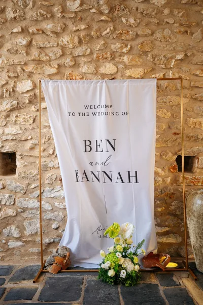 Wedding welcome sign as fabric wedding signage draped on a metal frame, set against a stone wall and floor.