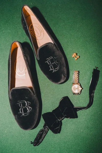 Groom shoes, black velvet loafers with monogram embroidery, set on green fabric for a refined, personalized touch.