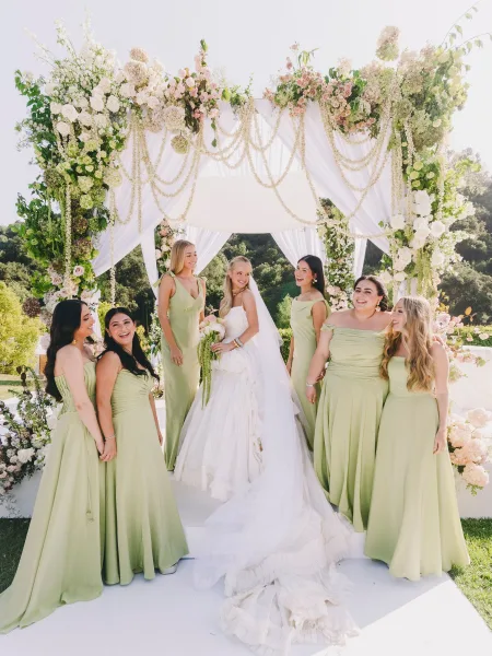 Bride and bridesmaids in sage green bridesmaid dresses pose closely, centering the bride and showcasing a cohesive wedding palette.