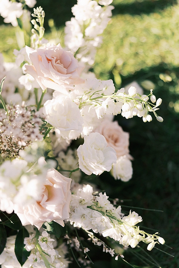 Wedding flowers with blush and white wedding flowers arranged with greenery on a sunlit garden lawn, airy and romantic close-up
