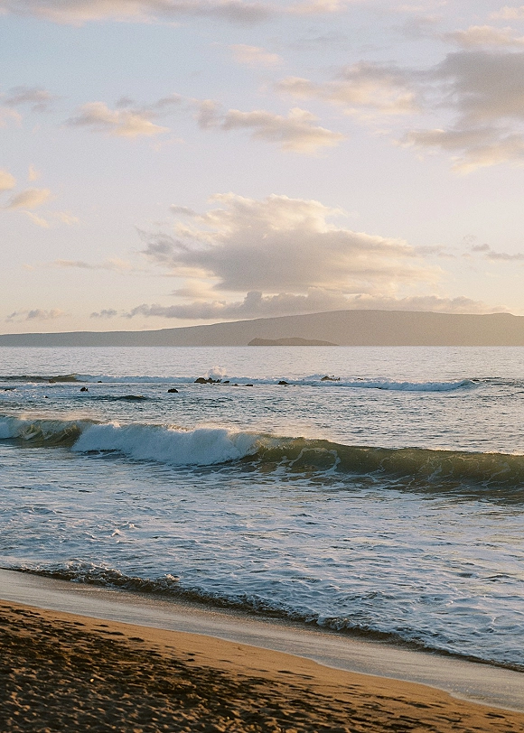 Beach landscape with ocean waves and sea foam rolling onto a sandy shoreline, with a distant island on the cloudy horizon