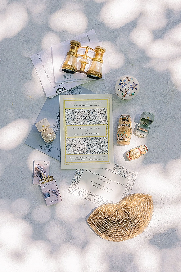 Invitation suite wedding invitation flat lay with blue and white cards, rings in a velvet box, pearl clutch on gray surface with sunlight shadows