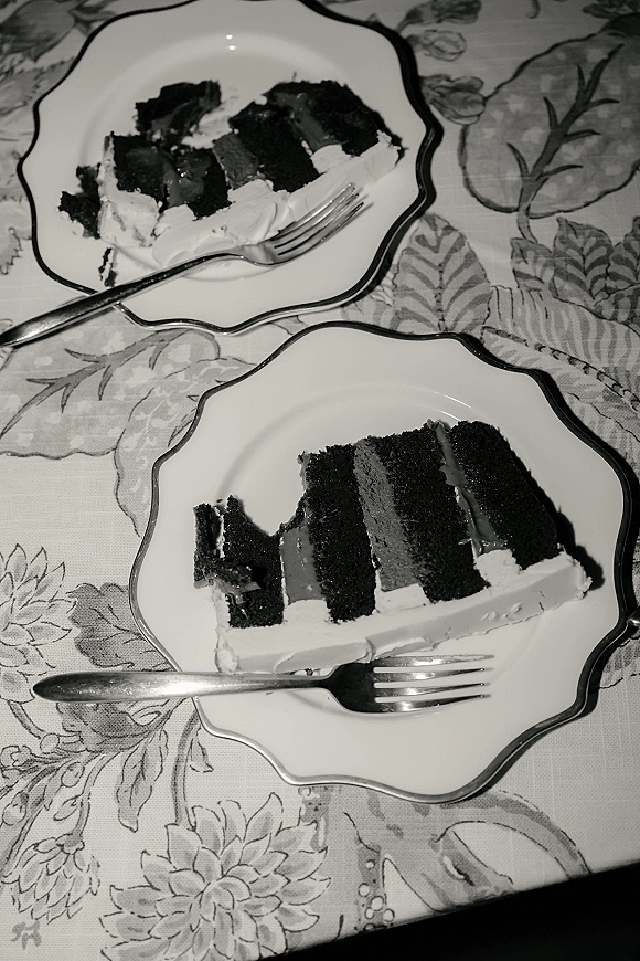 Wedding cake slices on scalloped dessert plates with forks, showing frosting and filling on a floral tablecloth tabletop setting