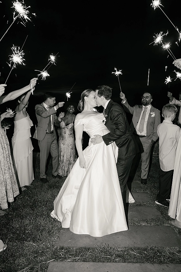 Wedding kiss portrait during a sparkler exit wedding, groom dipping the bride in her gown as guests hold sparklers under the night sky