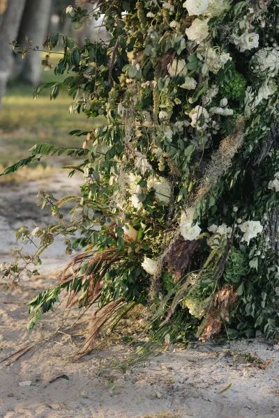 Wedding ceremony florals with a ceremony floral installation of white roses and lush greenery cascading on a tree trunk in an outdoor park setting