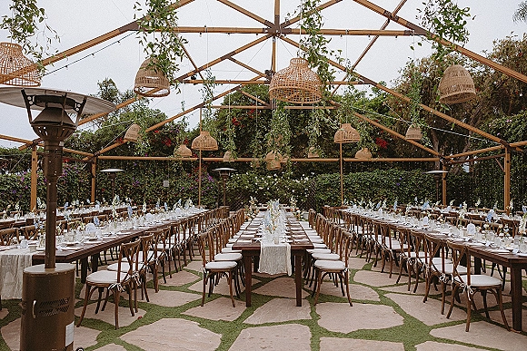 Reception tablescape with long banquet tables wedding featuring white runners, low florals and taper candles under rattan pendant lamps and string lights