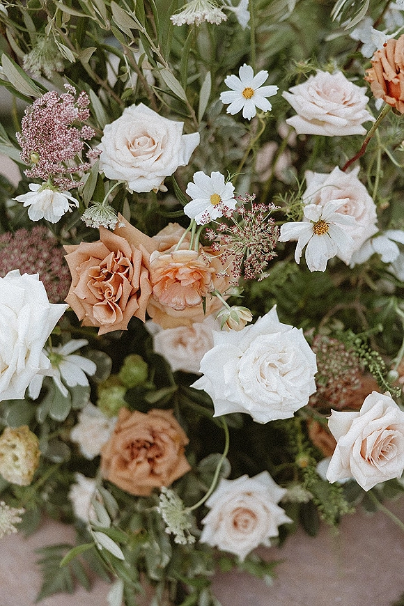 Bridal bouquet of white and peach bouquet roses with daisy accents and airy greenery arranged on a neutral surface