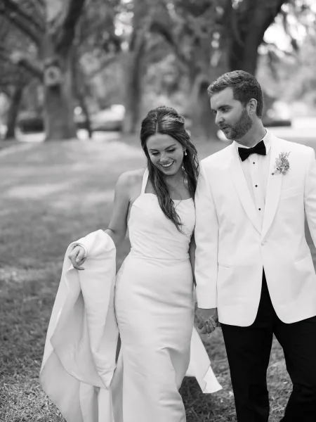Couple portrait in a black and white wedding portrait, bride and groom holding hands and walking on a lawn under oak trees in a park