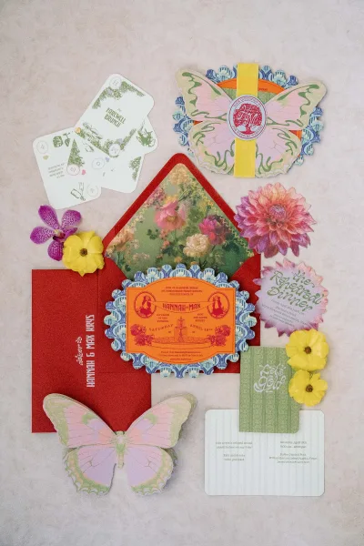 Invitation suite of colorful wedding invitations with butterfly cutouts, ribbon, wax seal, and floral cards on a light marble surface
