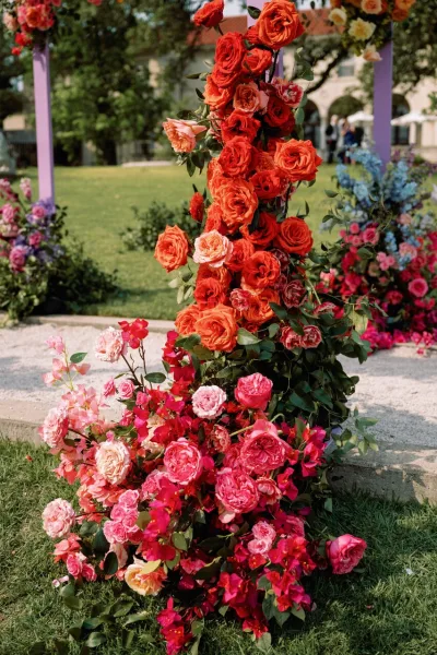 Wedding floral arch with rose wedding arch blooms and lush greenery on an asymmetrical frame, set on lawn by a garden path and facade