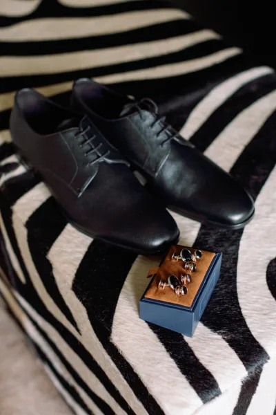 Groom accessories flat lay with black leather dress shoes and groomsmen gift cufflinks in a box on zebra print fabric backdrop