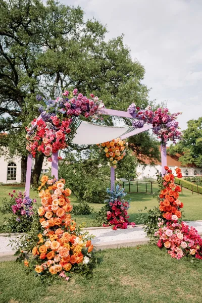Wedding ceremony arch with a colorful floral wedding arch of roses and hydrangeas, draped fabric canopy and ribbons on a garden lawn