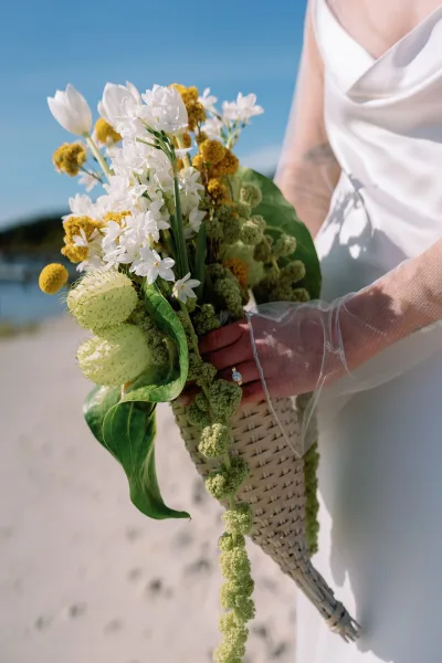 Bridal bouquet with wildflower bridal bouquet in a wicker holder, yellow and white blooms and trailing amaranthus, held on a sandy beach