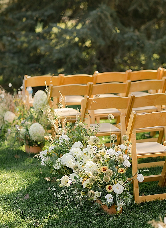Ceremony aisle decor with outdoor ceremony chairs, wood folding seats, and low white hydrangea florals in terracotta pots on a sunlit lawn