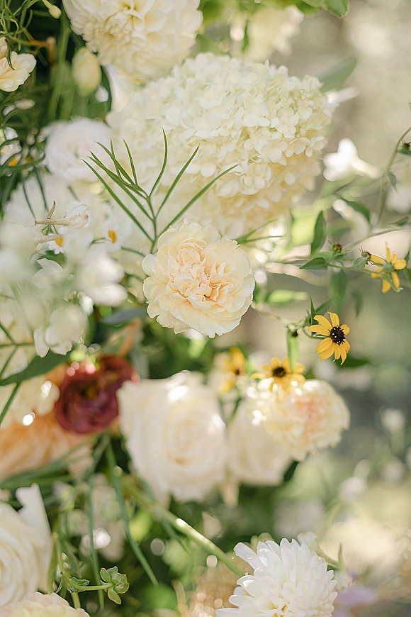 Wedding floral arrangement with white hydrangea centerpiece, white and blush roses and greenery, softly lit by sunlight outdoors