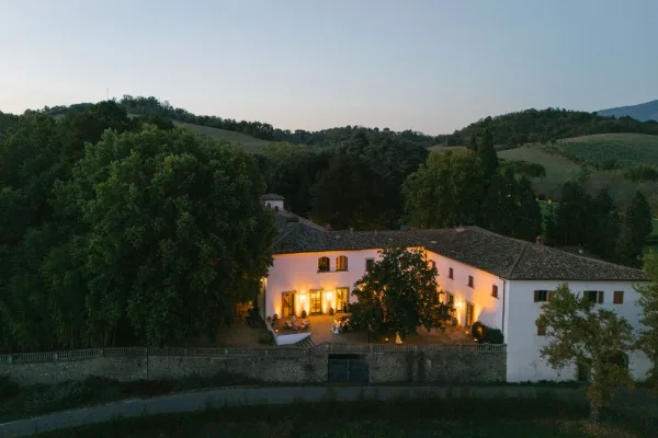 Wedding venue exterior with warm string lights over patio lounge seating beside a stone wall, set against countryside hills at twilight