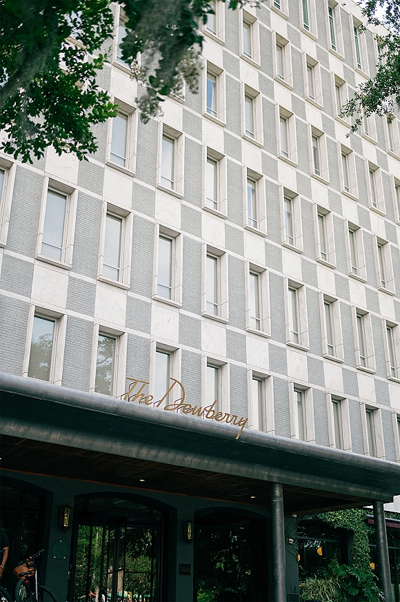 Wedding venue exterior with boutique hotel entrance canopy and glass doors, featuring hotel sign lettering on a brick facade with greenery
