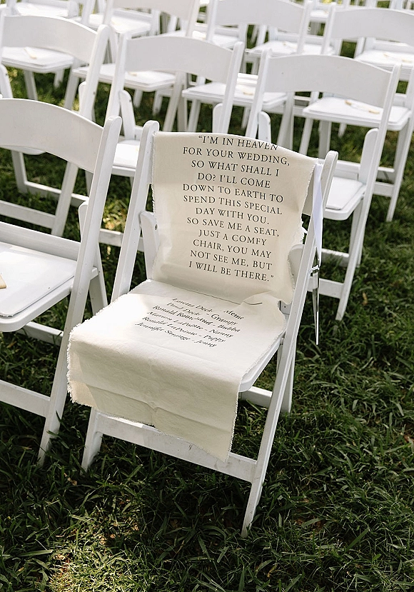 Wedding memorial seat with a memorial sign and soft fabric drape on a white folding chair among outdoor ceremony seating on grass lawn