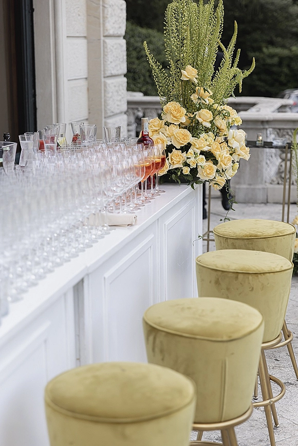 Wedding bar setup with wedding cocktail hour bar featuring champagne coupe glasses, rosé, and yellow rose greenery florals on a stone terrace