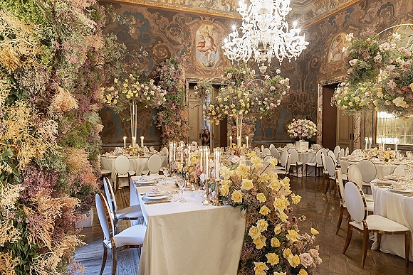 Reception tablescape with luxury wedding reception details, tall rose centerpieces, taper candles, gold-rimmed plates under hanging florals and murals