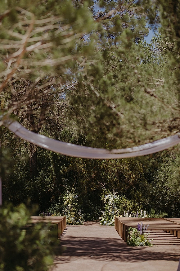 Ceremony aisle design for an outdoor ceremony aisle with wood bench seating, blue and white florals, and fabric draping in pine forest