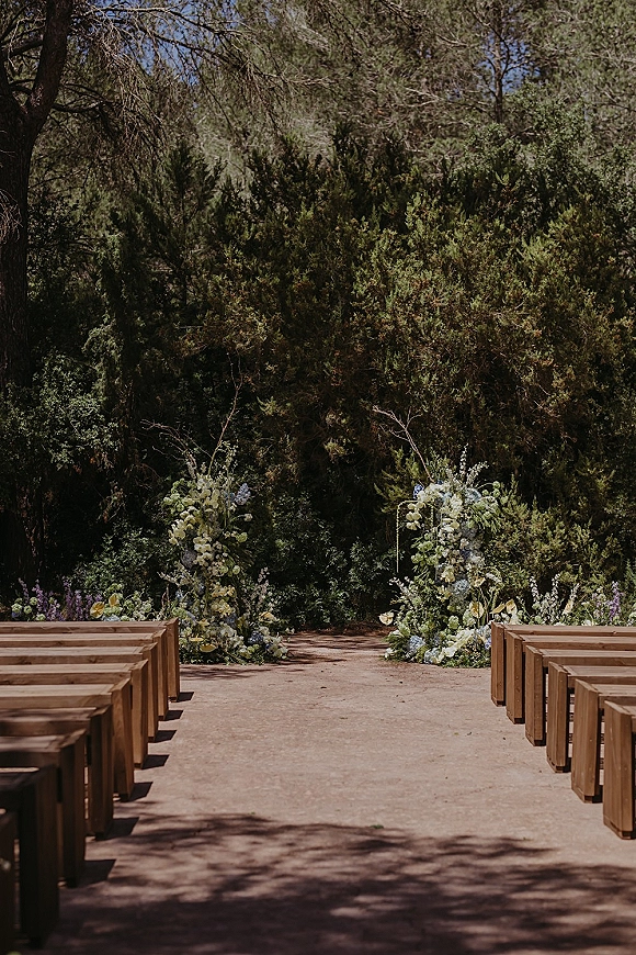 Ceremony aisle decor with an outdoor ceremony aisle lined by wood benches, greenery, and ground florals in a garden setting