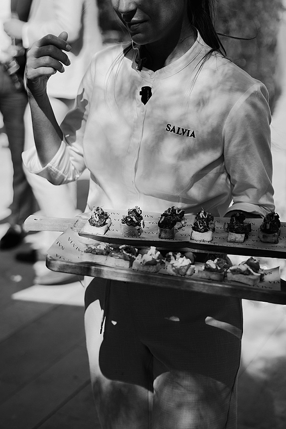 Wedding cocktail hour with passed appetizers on wooden serving boards and a canapé tray as guests mingle on a sunlit outdoor patio