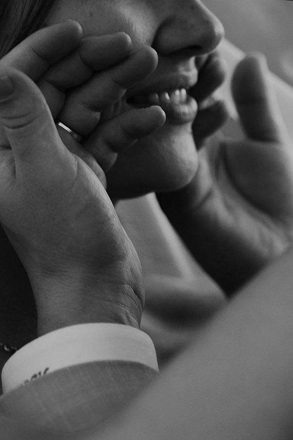 Wedding kiss portrait in a black and white wedding photo, groom holding bride’s face with wedding ring visible against a blurred indoor background