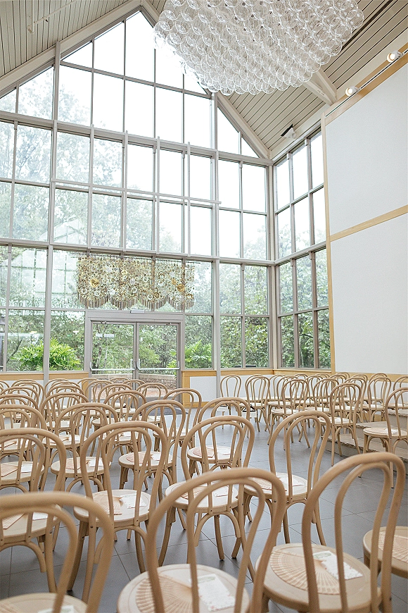 Ceremony seating with wedding ceremony chairs in neat rows of wood chairs, place cards and a glass bubble chandelier under vaulted windows