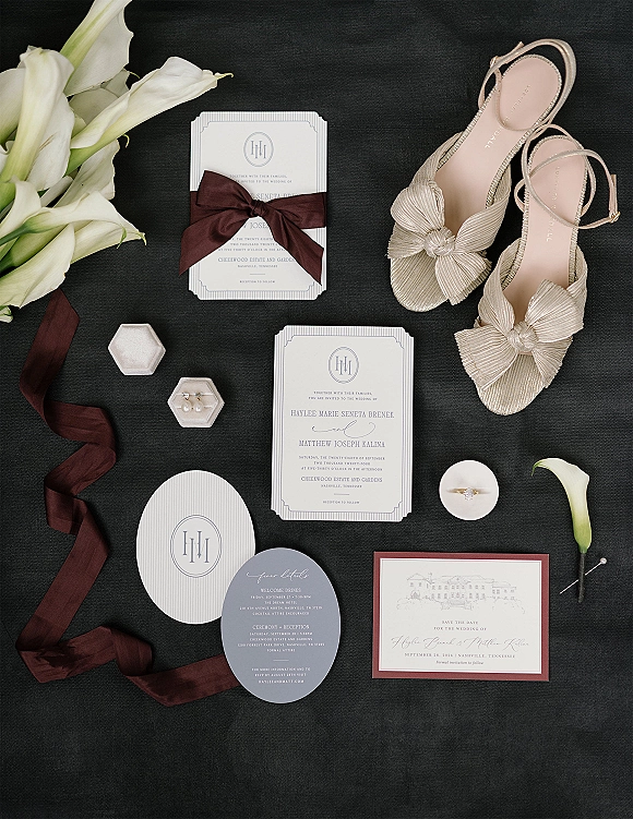 Wedding invitation suite wedding flat lay with calla lilies, silk ribbon wrap, engagement ring, pearl earrings and bow heels on black fabric backdrop