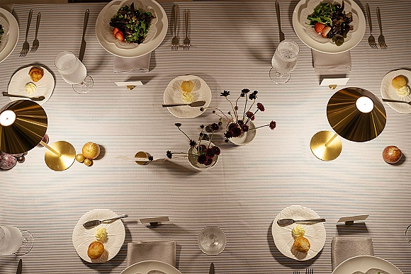 Reception tablescape with wedding place setting on a striped tablecloth, layered white plates, folded napkins, place cards, and brass table lamps